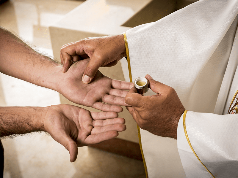 Un prêtre baptise un adulte. Onction du Saint Chrême sur les mains.